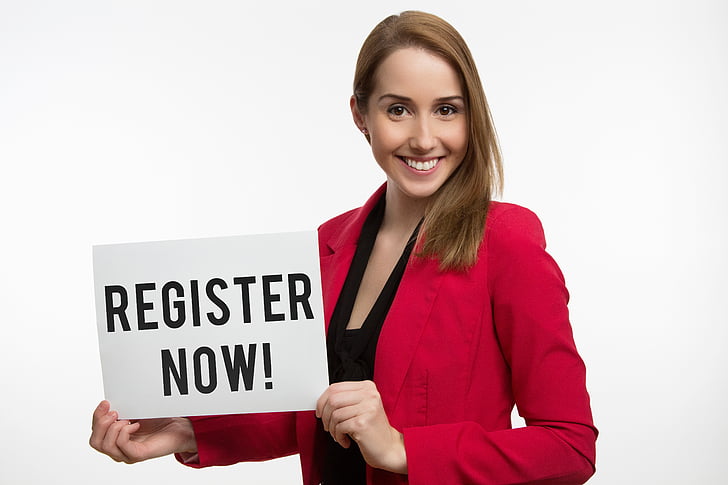 woman wearing red blazer holding register now signage