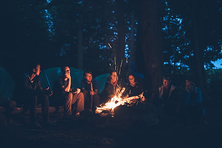 bonfire surrounded by group of men near tents and trees
