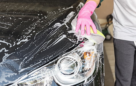 person wearing pink rubber glove washing black car