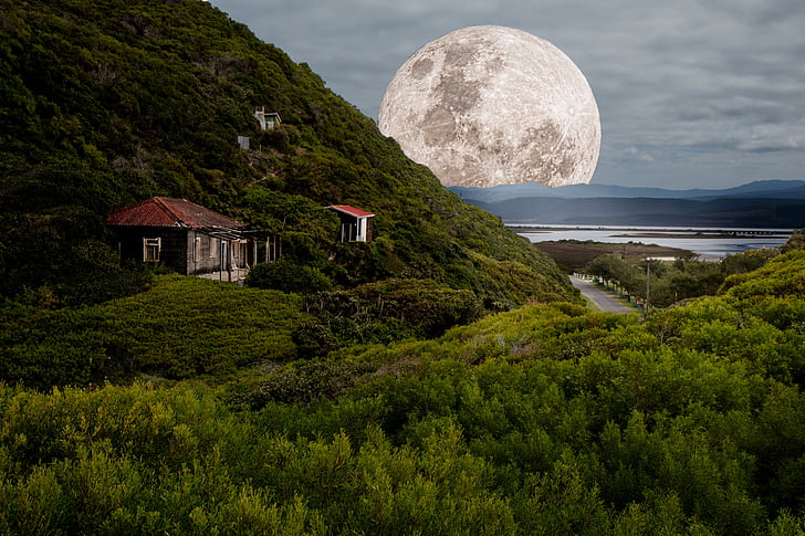 house on cliff and moon at distance during daytime