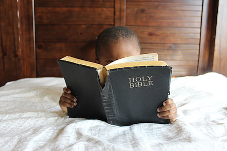 boy lying on bed reading Holy Bible