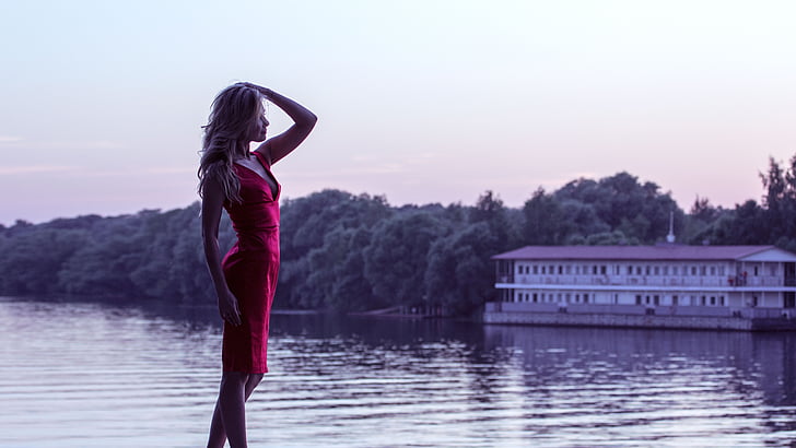 woman wearing red mini dress standing beside body of water during golden hour