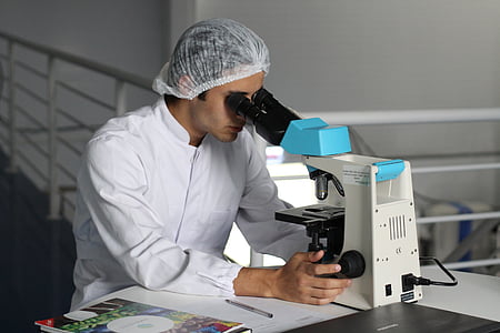 man in white long-sleeved shirt while using microscope