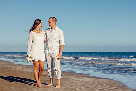 woman in lace long-sleeved mini dress with man in white dress shirt standing on seashore during daytime