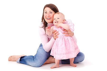 woman in pink long-sleeved top and blue jeans sitting on floor with infant in pink dress