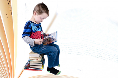 toddler in Spiderman printed shirt sitting down on pile of books reading book