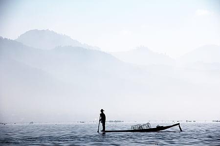 silhouette of man standing on boat near mountain