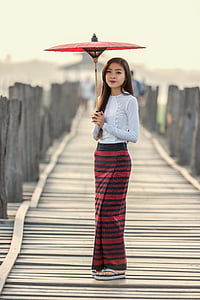 focus photography of a woman standing on bridge wearing white long-sleeved shirt holding oil umbrella