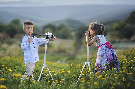selective focus photography of boy and girl on flower field using while standing near cameras with tripods