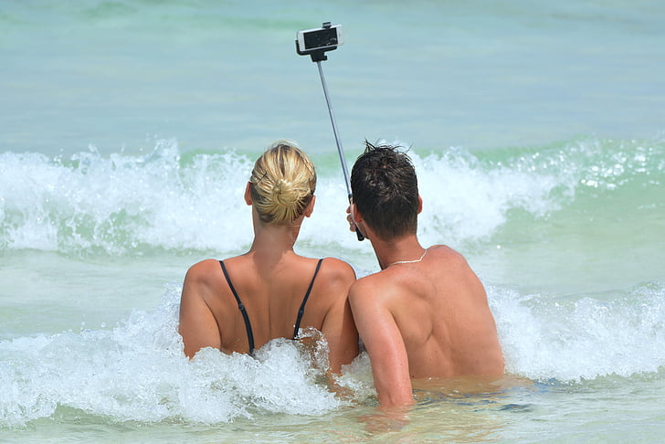 man and woman on beach taking selfie using monopod stick