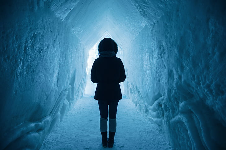 person in winter jacket standing inside the ice cave