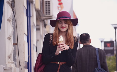 woman wearing sun hat holding ice cream near building