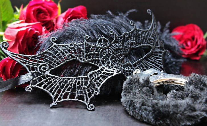 black masquerade mask surrounded by red Rose flowers