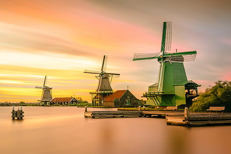 green windmill near body of water at sunset