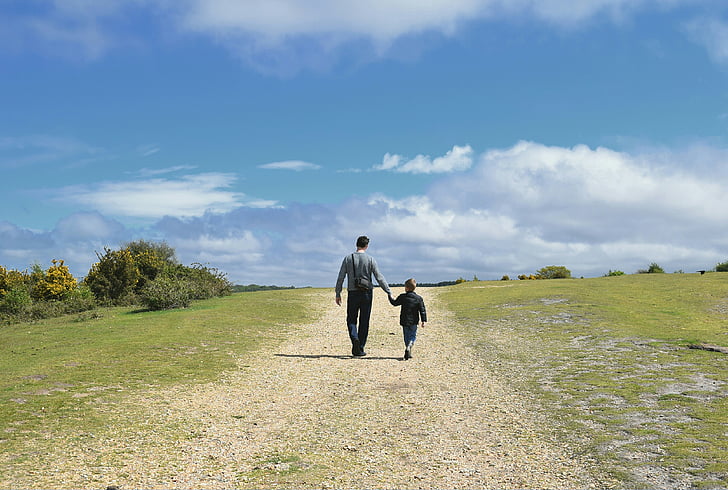 man holding children while walking on green grass field
