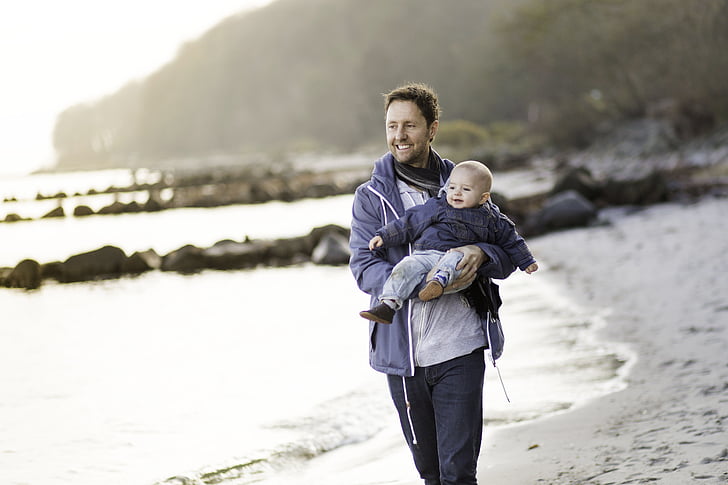 man carrying baby near seashore during daytime