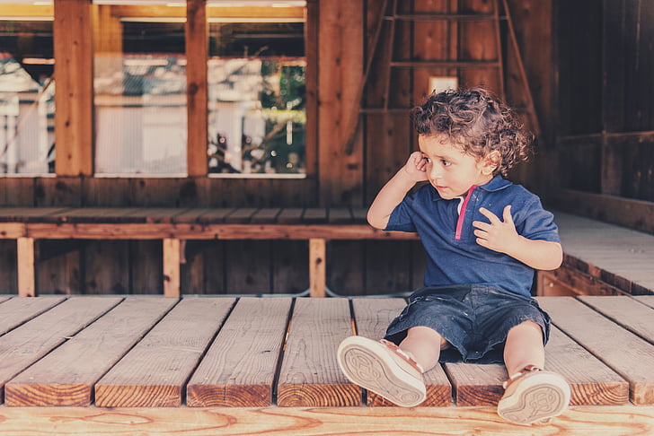boy in blue shirt sitting on wooden dock during daytime
