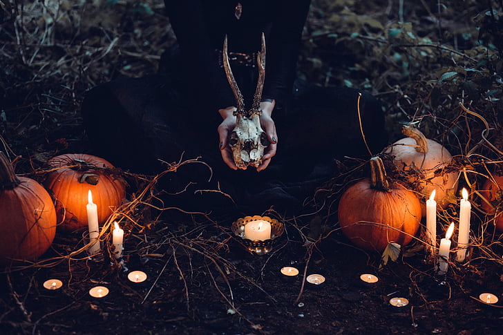 female laying on floor beside pumpkins with lighted candles