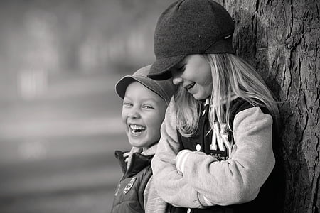 girl and boy leaning on tree trunk grayscale photo