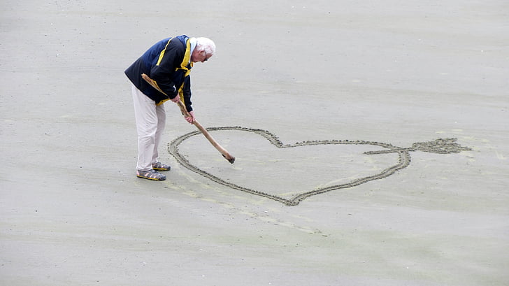 man sketching heart with arrow on sand \