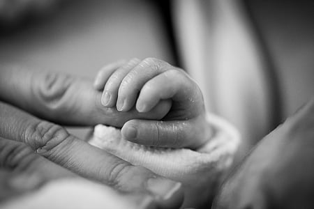 grayscaled photo of baby holding person's hand