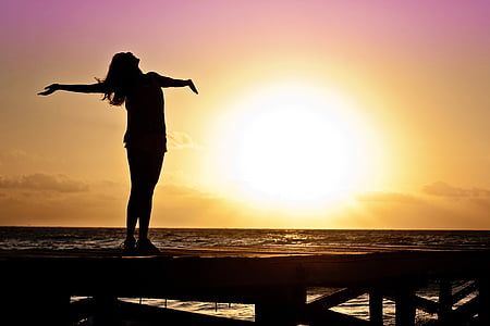 silhouette of woman spreading hand standing on port near body of water with sunset view