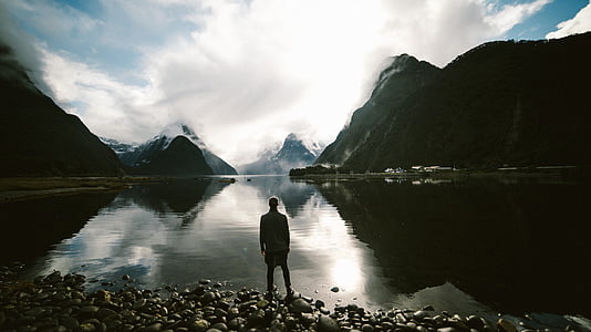 silhouette photo of man in front of water and mountain