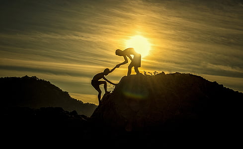 silhouette of man helping another man to climb on cliff during golden hour
