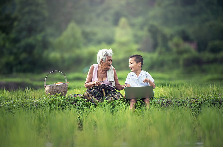 boy with laptop sitting beside white haired woman on green field