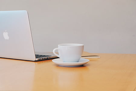 white ceramic teacup beside silver MacBook