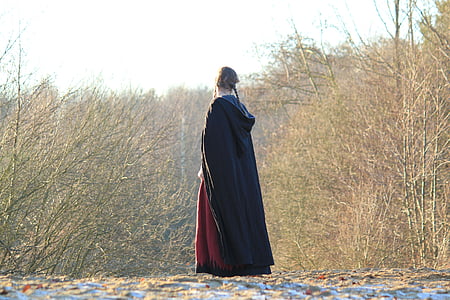 woman wearing black dress standing on pathway between brown trees