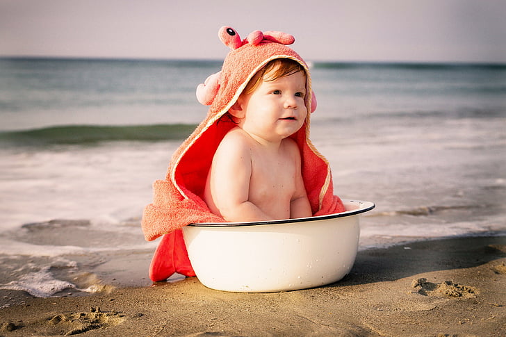 baby sitting on white basin on seashore